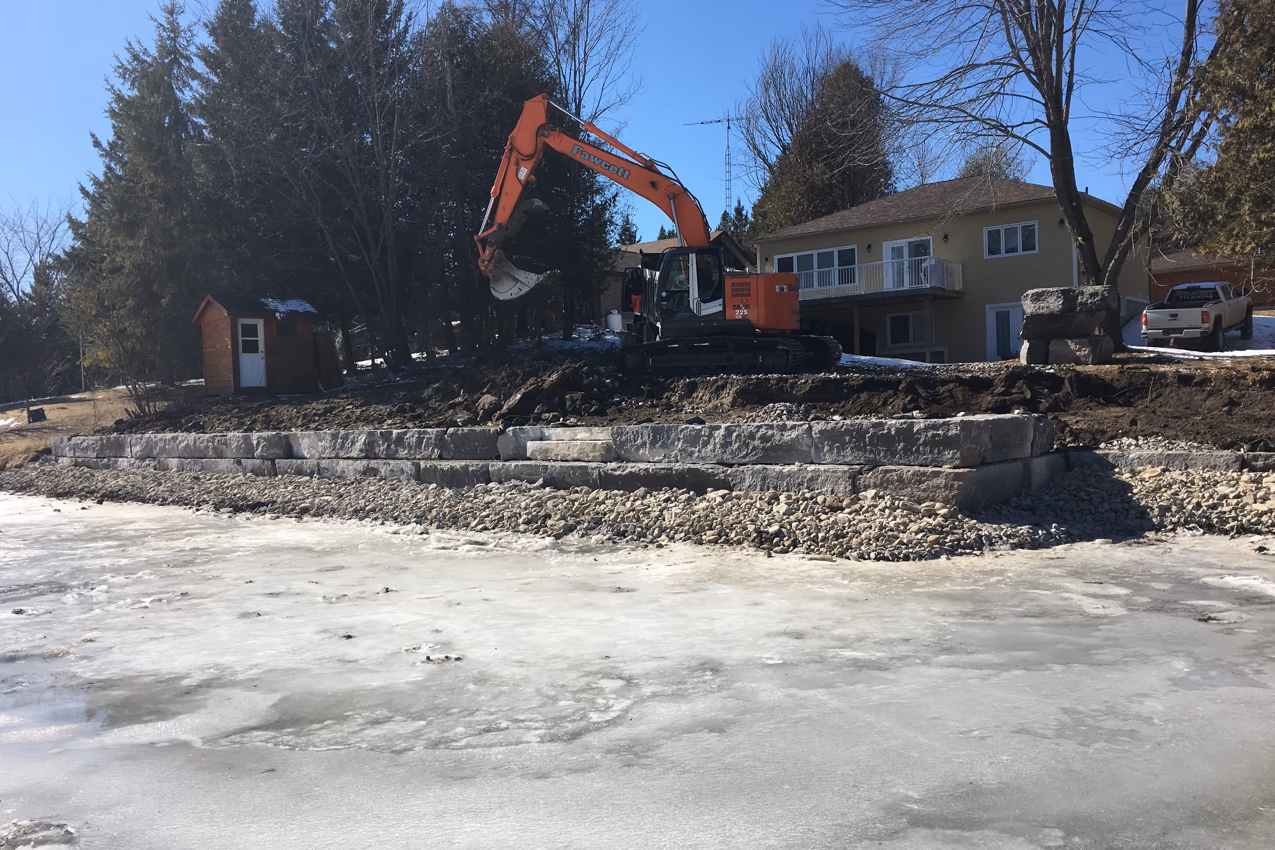 Excavator placing large rocks for shoreline protection on a Kawartha lake